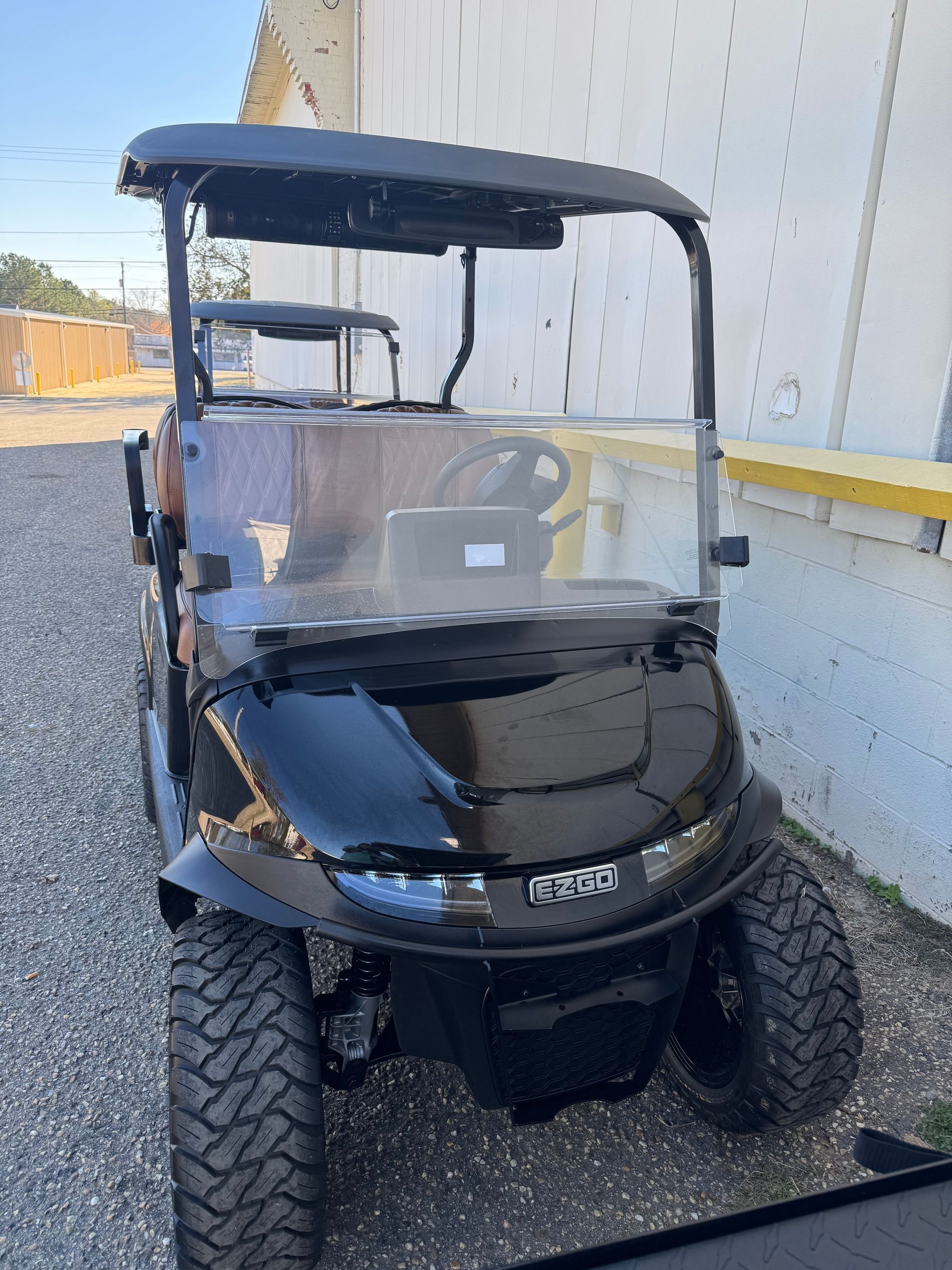 Black golf cart with clear windshield and black roof, parked outdoors.