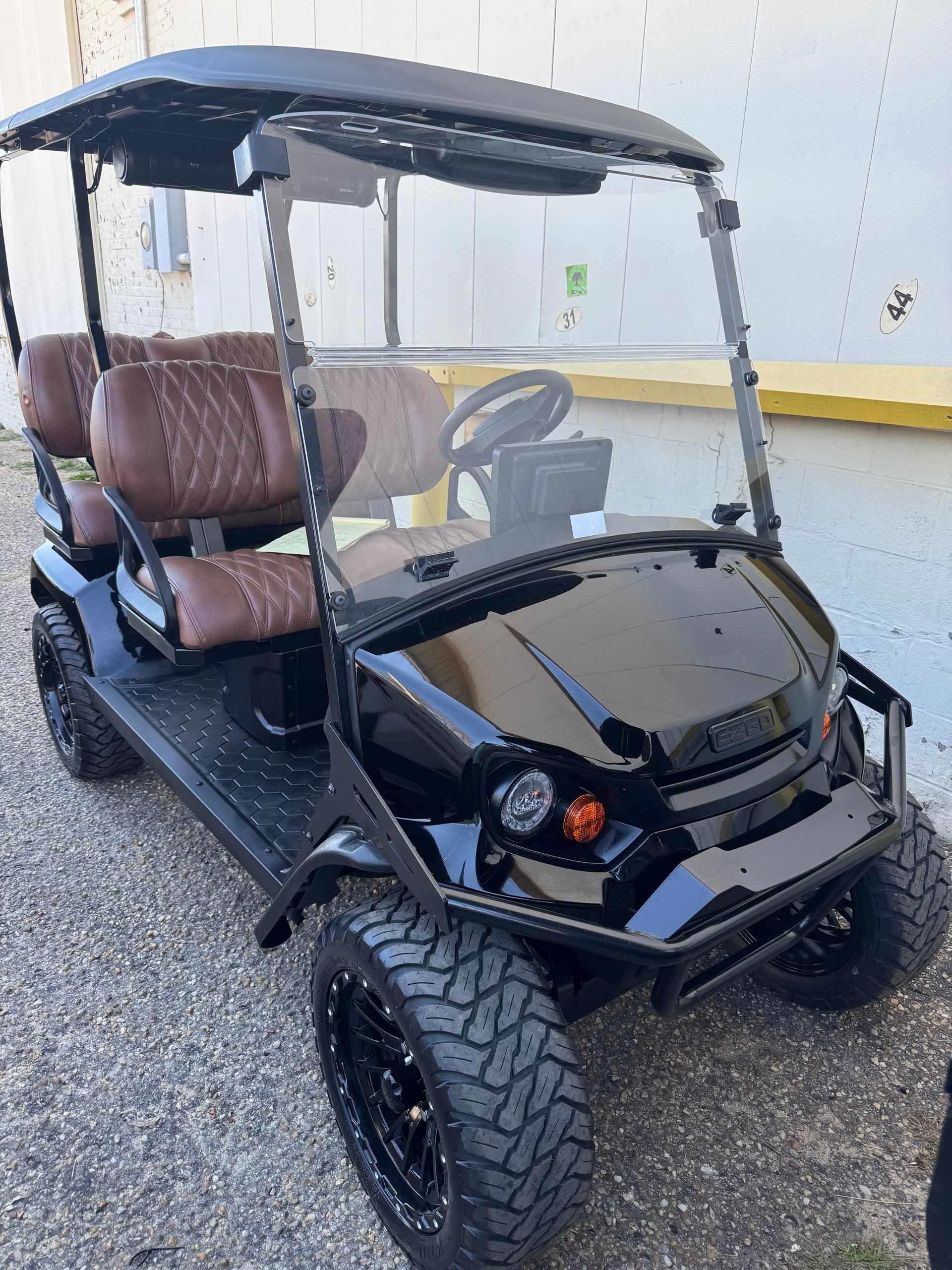 Black golf cart with brown seats and off-road tires, parked outside a building.
