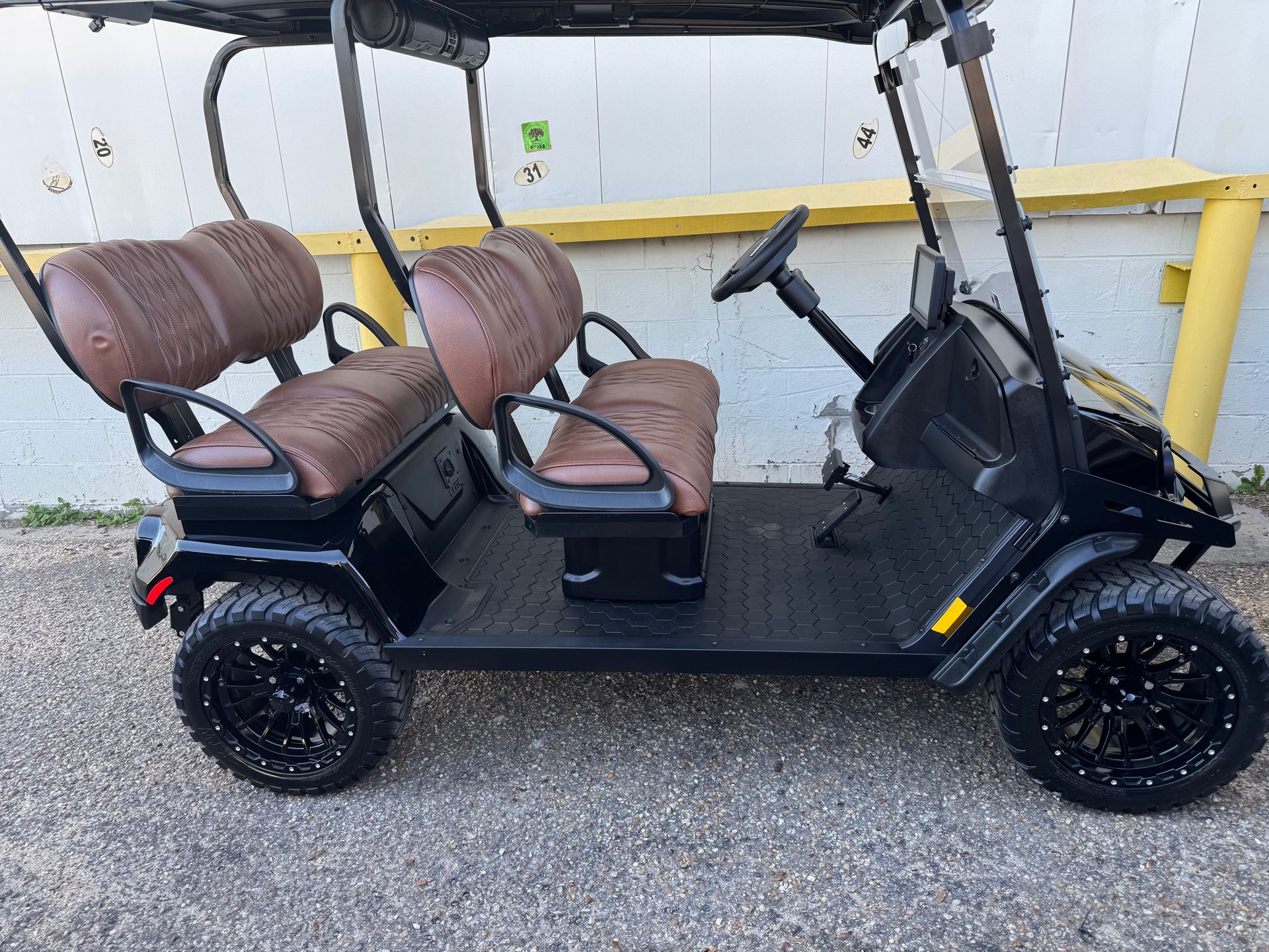 Black golf cart with brown seats and off-road tires, parked outside a building.