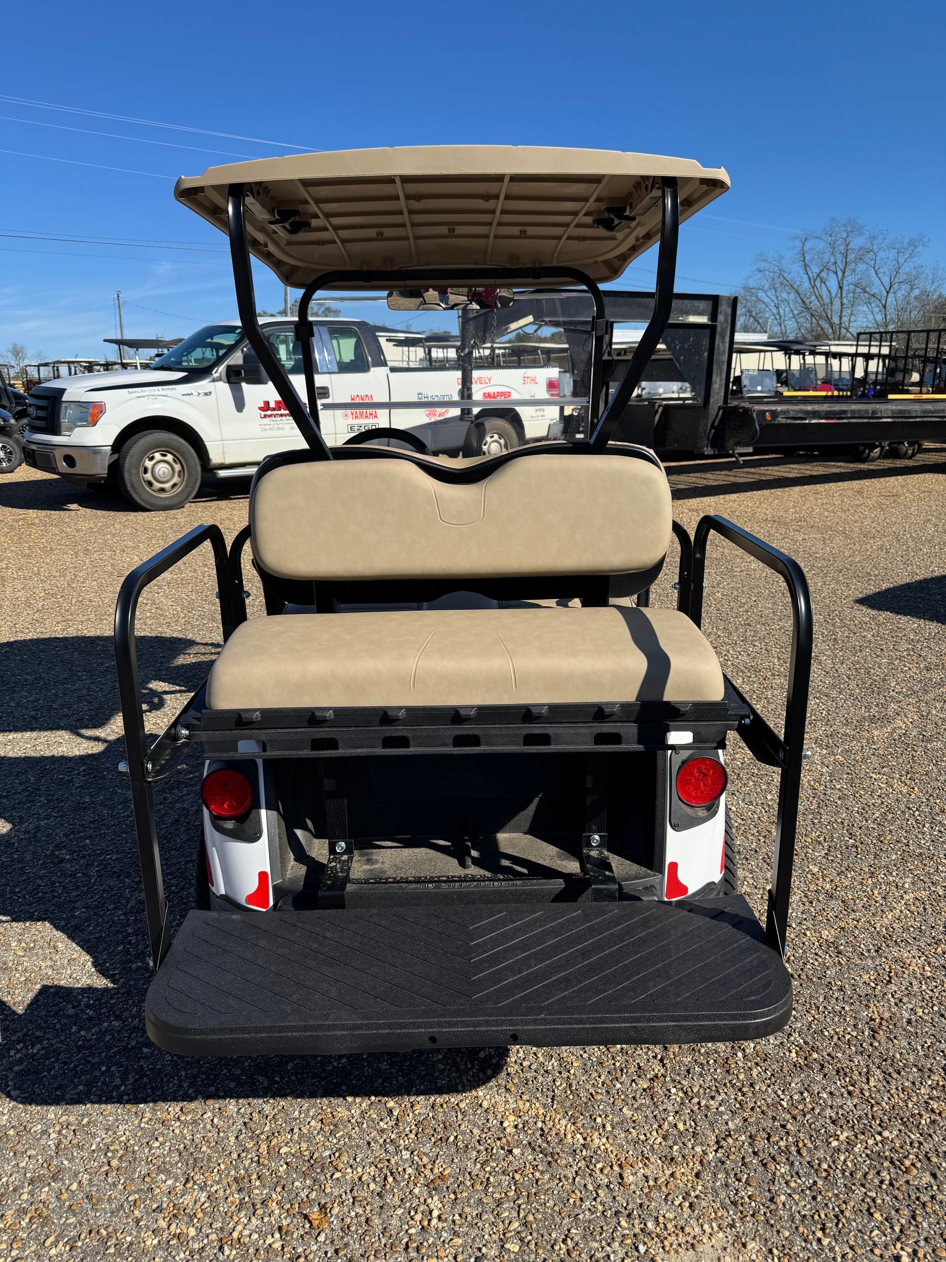 White golf cart with tan roof and seats on a paved lot on a sunny day.