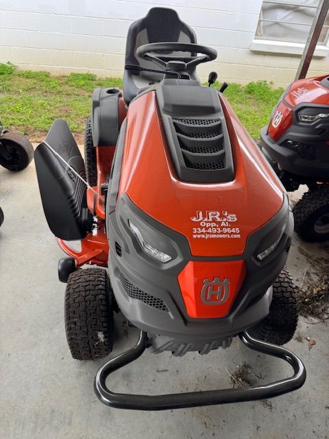 Orange and gray Husqvarna riding lawn mower with black tires and seat, parked outside.