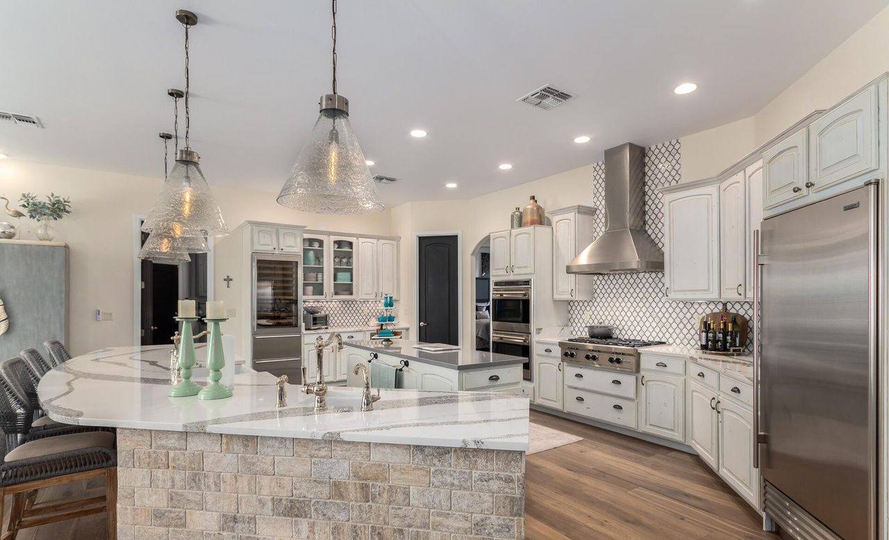 Spacious, white kitchen with a curved island, stainless steel appliances, and pendant lights.