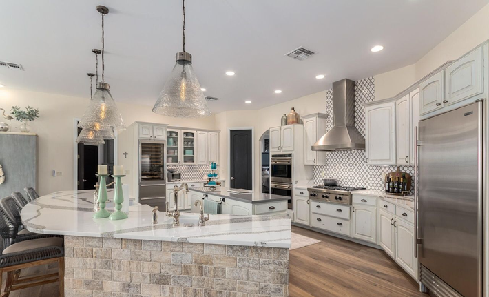 Spacious, white kitchen with a curved island, stainless steel appliances, and pendant lights.
