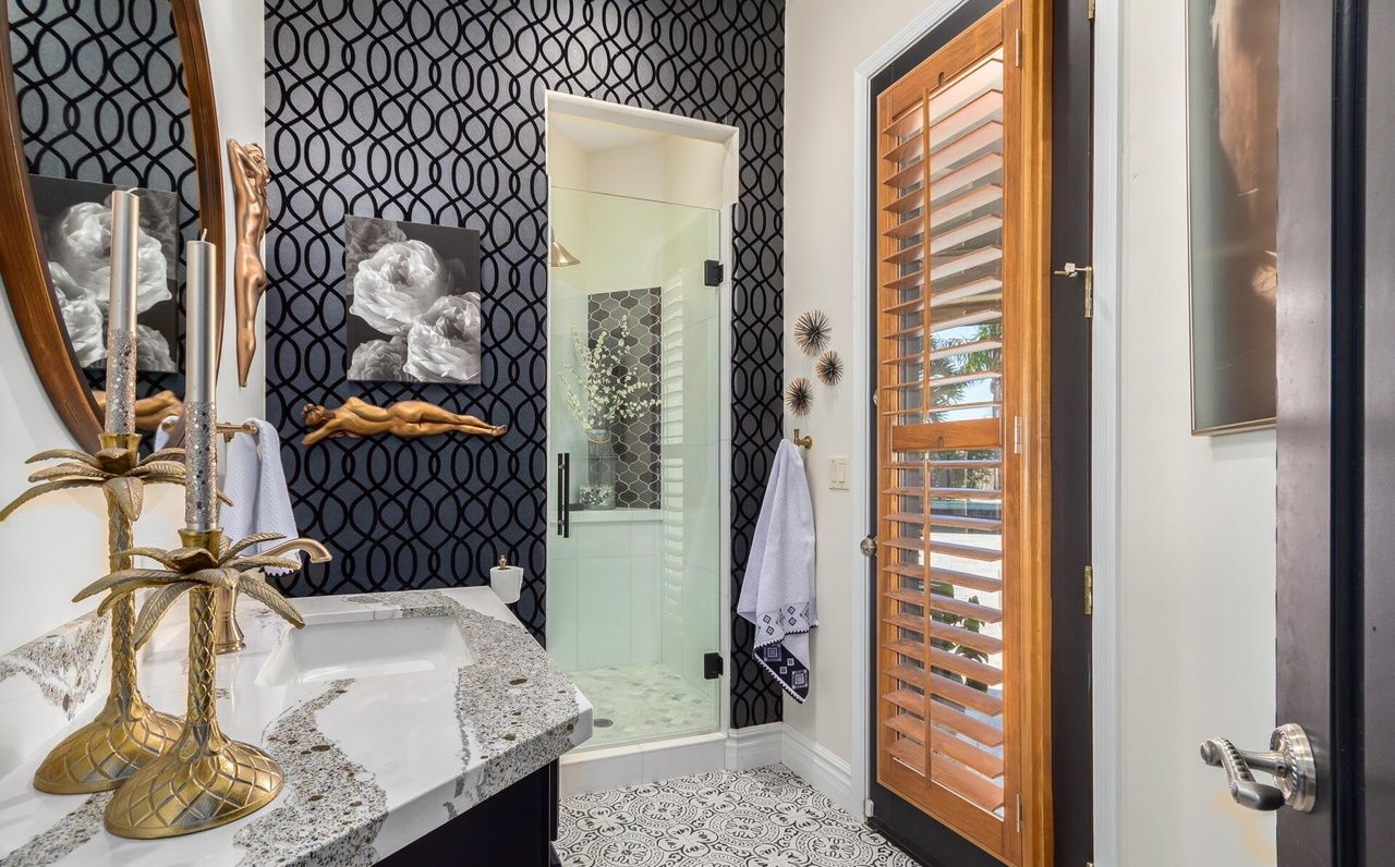 Bathroom with a dark patterned wall, glass shower, and wooden shutter door.