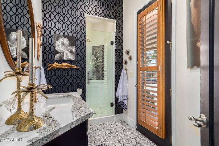 Elegant bathroom with patterned wallpaper, glass door, and wood shutters.