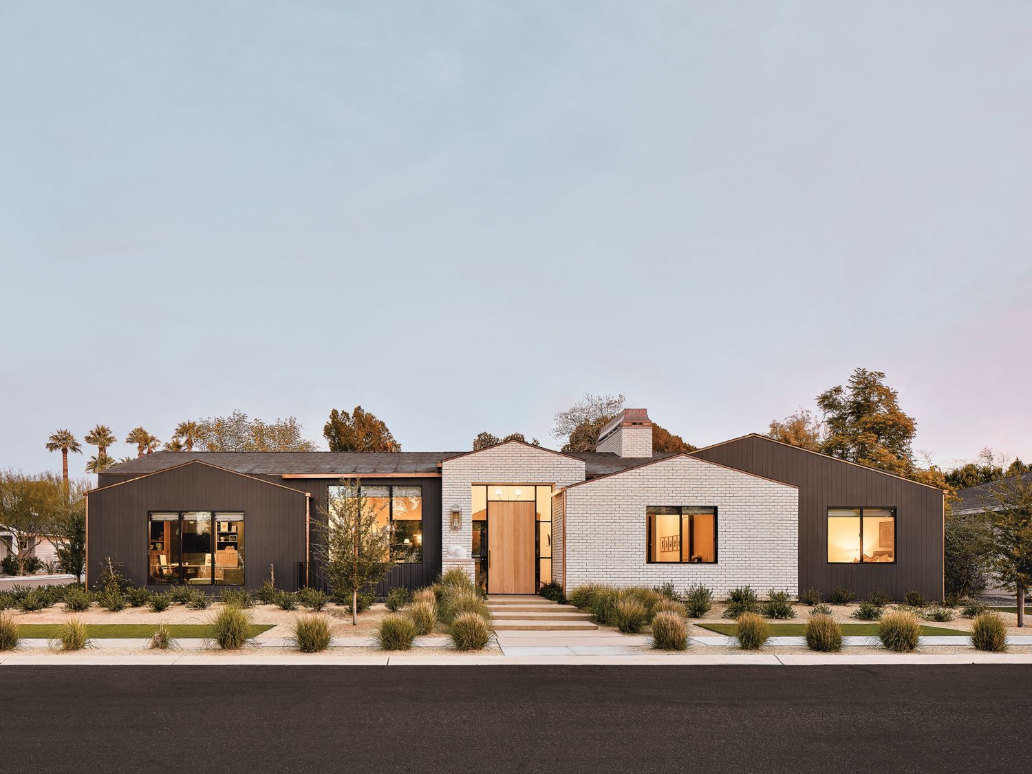 Modern home with dark gray and silver brick exterior, walkway, and landscaping under a dusk sky.