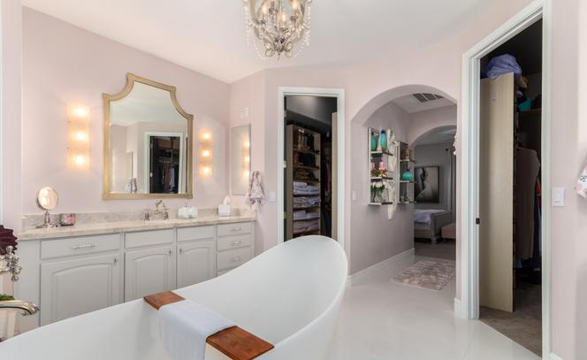 Elegant bathroom with a white tub, light pink walls, and a large mirror.