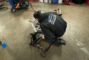 Person kneeling beside a small dirt bike in a workshop, adjusting the engine area | Retana's Auto Repair LLC