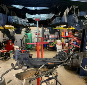Car under repair on a lift in an auto shop, with a detached front suspension and tools below.