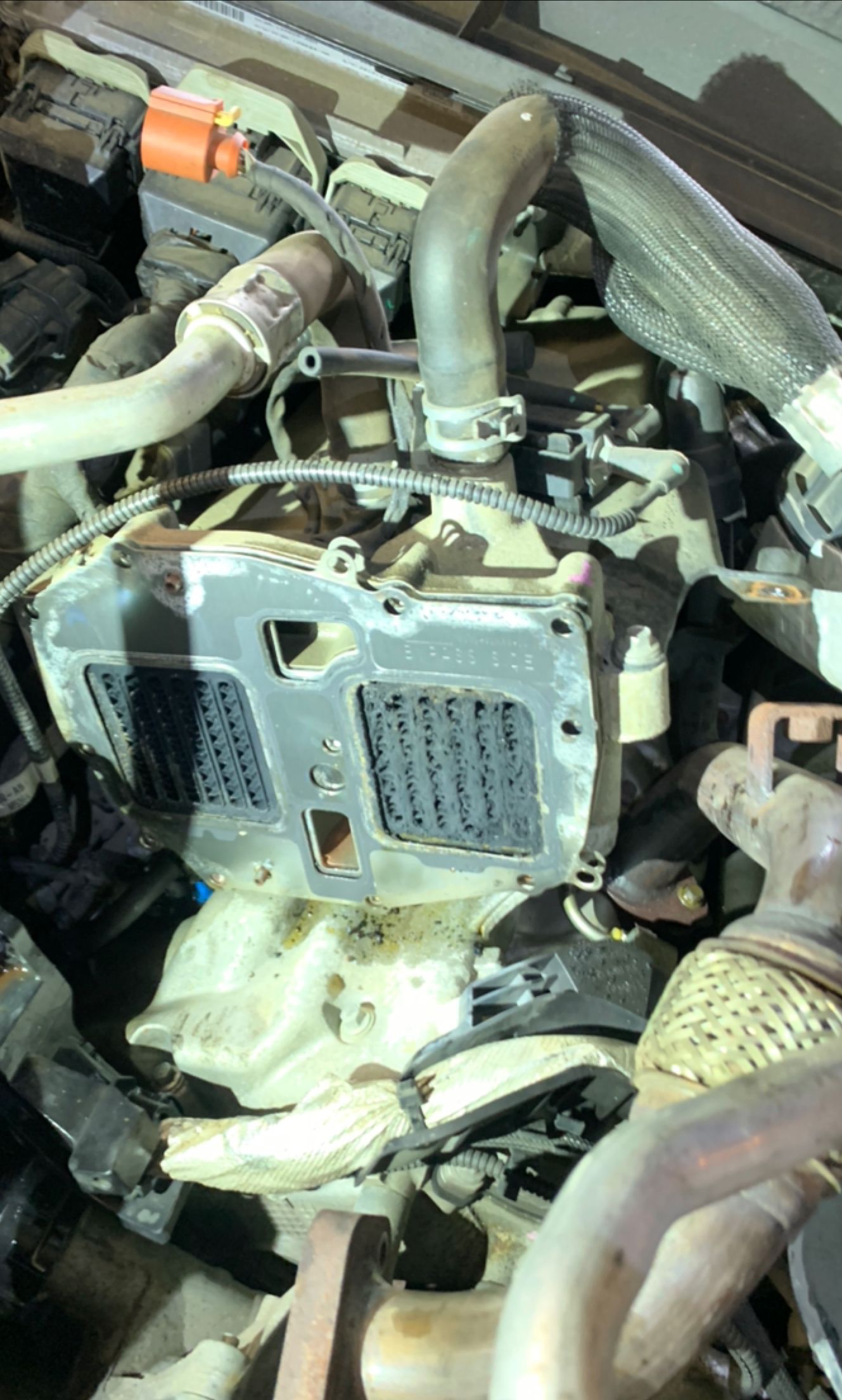 Close-up of a vehicle engine bay with hoses, wiring, and a metal control module.