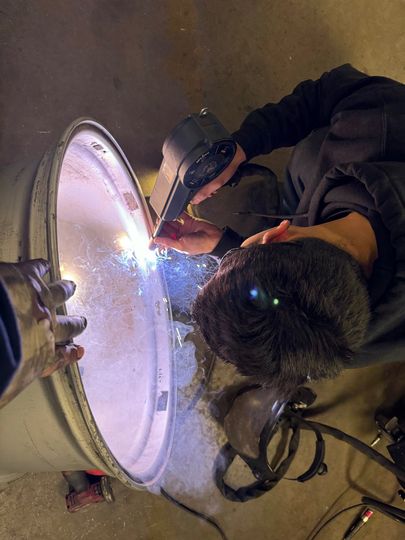 Worker welding a large metal tank, sparks flying in a dim industrial setting | Retana's Auto Repair LLC