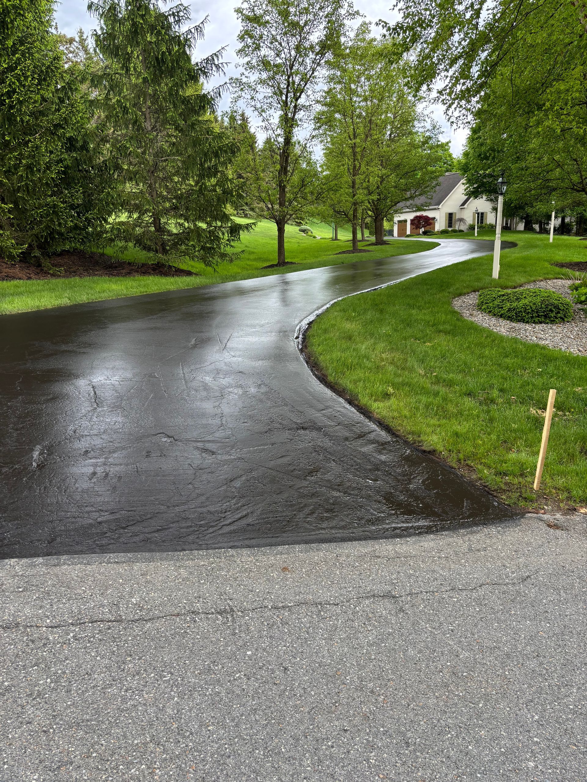 A curvy driveway leading to a house surrounded by trees and grass.