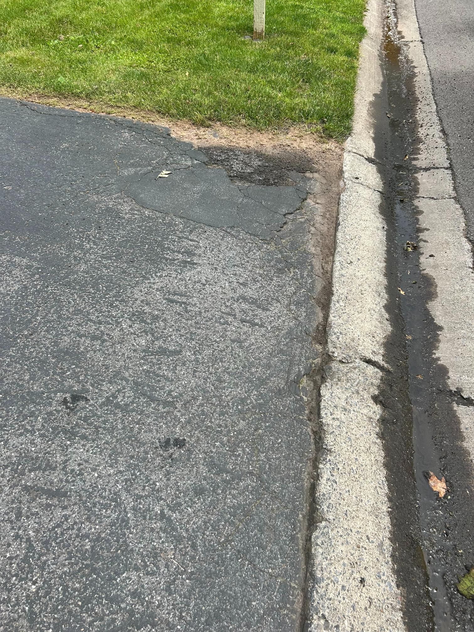 A drain on the side of a road next to a grassy area.