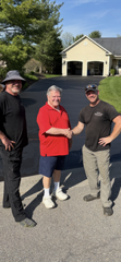 Three men are shaking hands in front of a house.