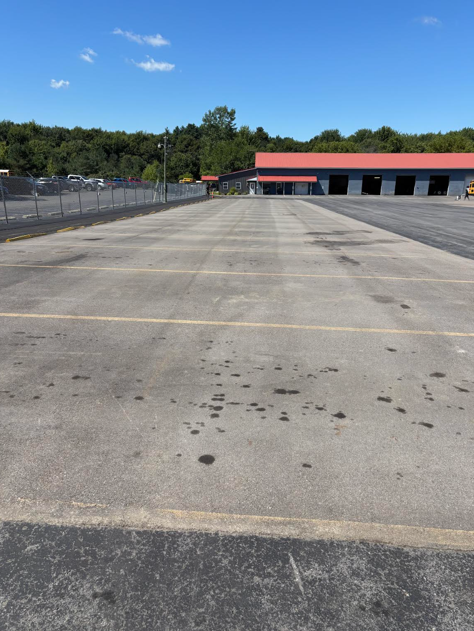 Empty asphalt parking lot on a sunny day with a red-roofed building in the background.