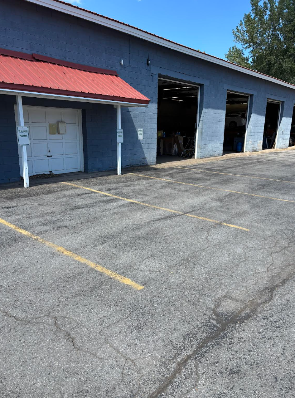 Blue building with red awning and open garage bays; parking lot in front.