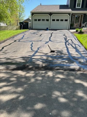 A driveway with cracks in it is being painted in front of a house.