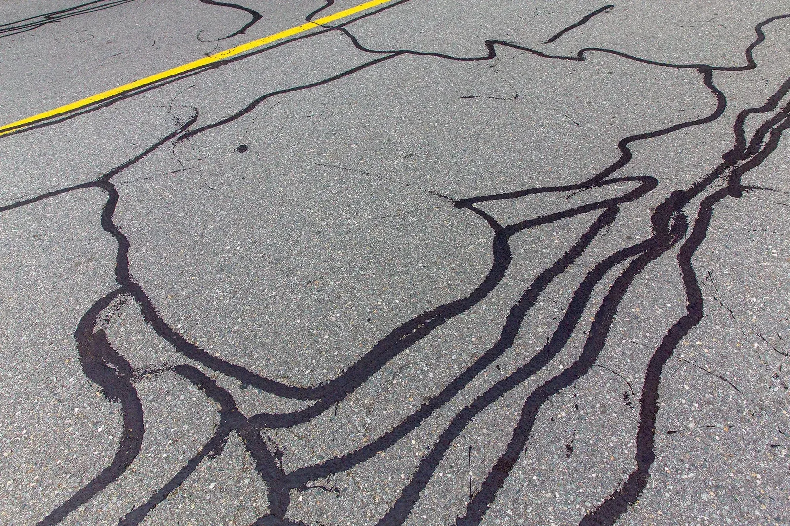 A close up of a cracked asphalt road with a yellow line.