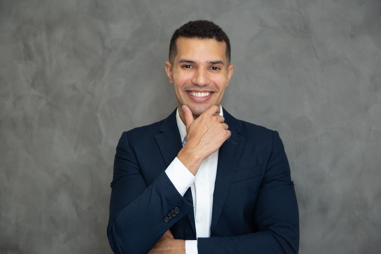 Um homem de terno e gravata está sorrindo com a mão no queixo.
