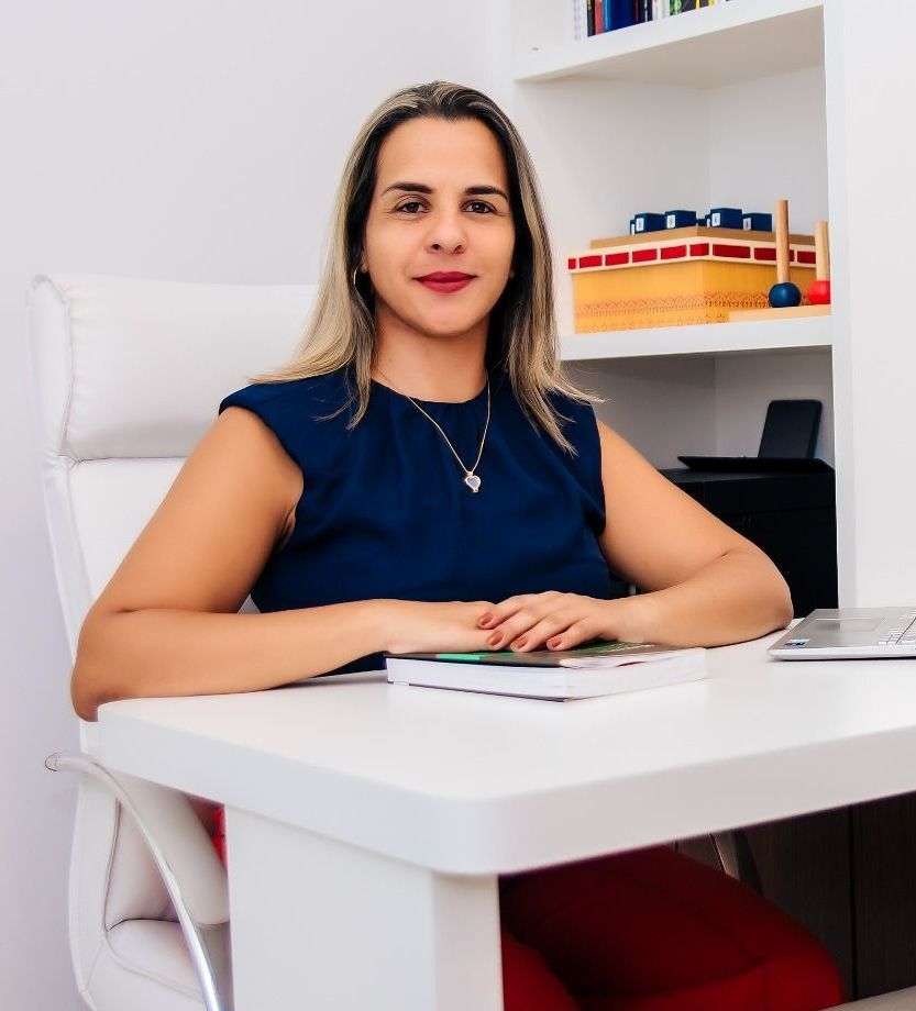 Uma mulher com uma camisa floral preta e branca está sorrindo com os braços cruzados.