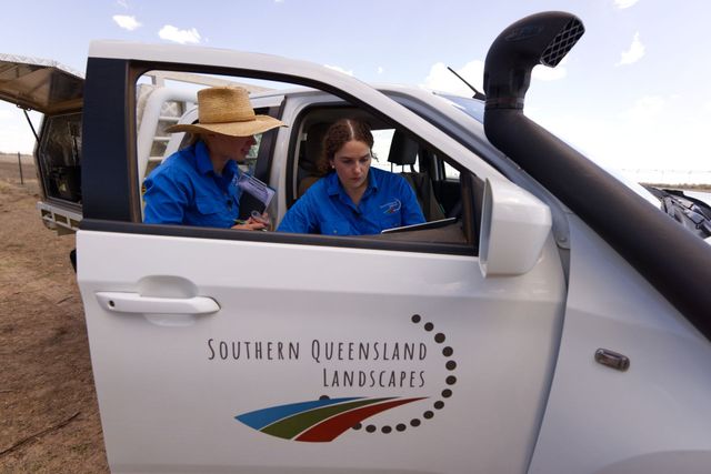 Two people in blue shirts sit in a white South Queensland Landscapes vehicle outdoors.