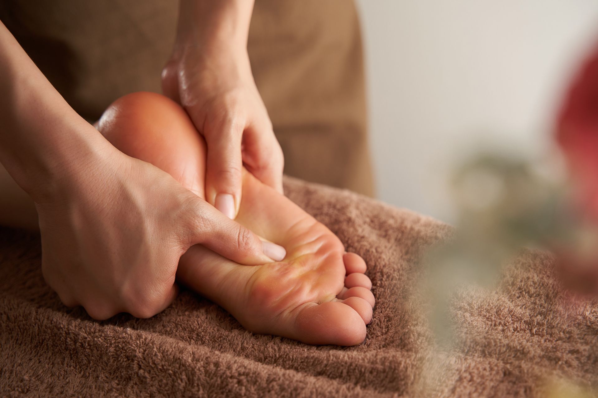 Hands massaging a bare foot on a brown towel, with a soft, warm background