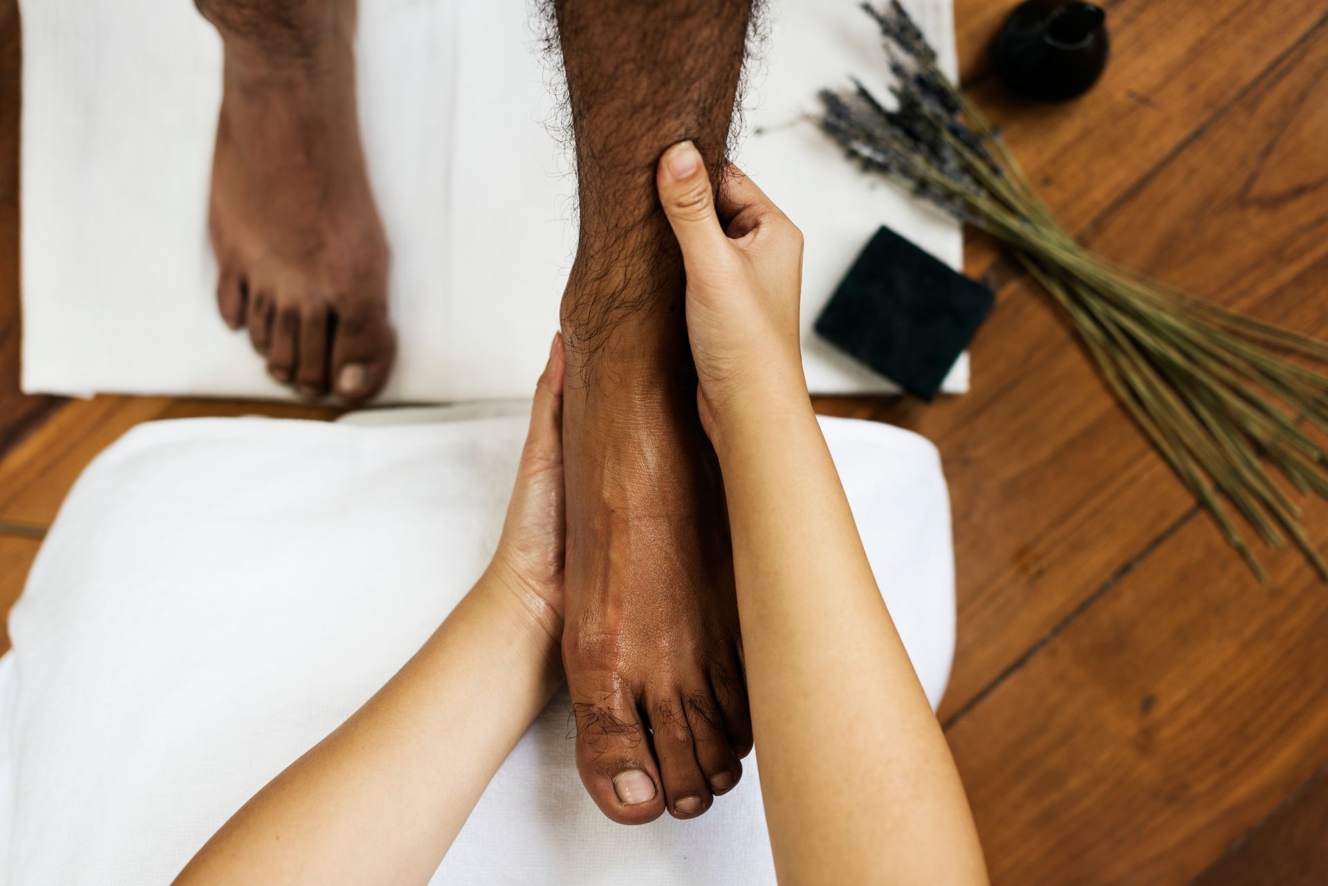 Hands massaging the foot of a dark-skinned person on a white towel.