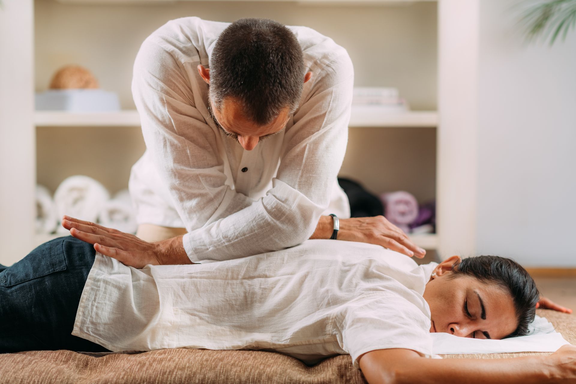 Person receiving back therapy, laying face down; therapist applying pressure with hands.
