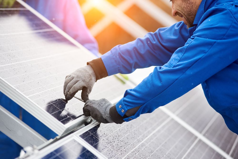 Worker in Blue Coveralls and Gloves Installing Solar Panels on a Roof — Level Electrical & Air In Taminda, NSW