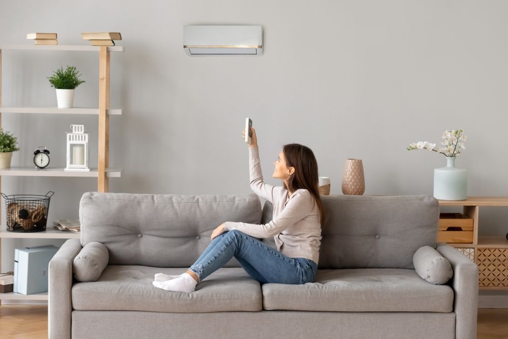 Woman Sitting on A Sofa, Using a Remote to Control an Air Conditioner — Level Electrical & Air In Taminda, NSW
