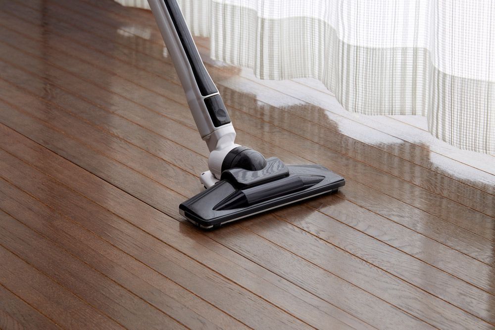 Vacuum Cleaner Cleaning a Wooden Floor Near a Window With Sheer Curtains — Level Electrical & Air In Taminda, NSW