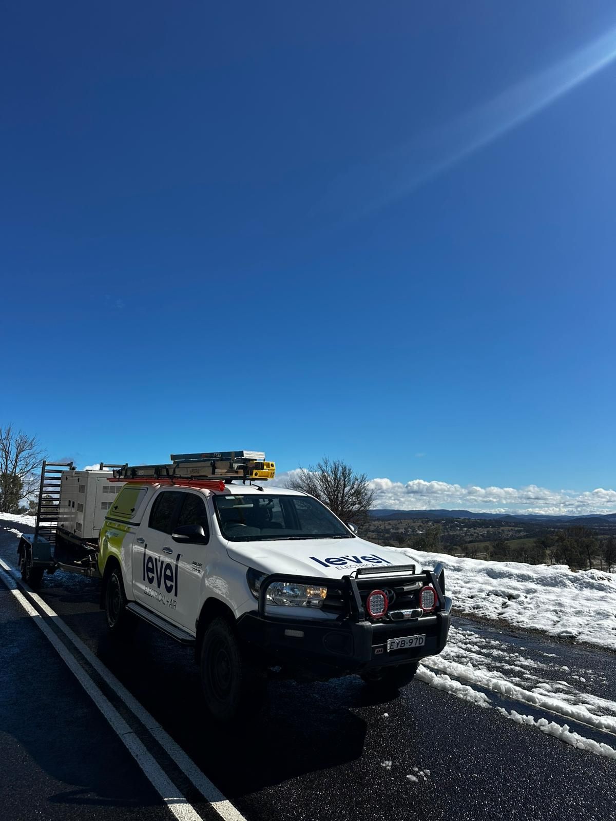 White utility truck parked on a snowy roadside under a bright blue sky with mountains in the distance — Level Electrical & Air In Taminda, NSW
