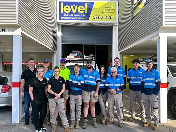 Staff group posing outside a Level Truck Repairs garage with blue signage and a tow truck in the bay  — Level Electrical & Air In Tamworth, NSW
