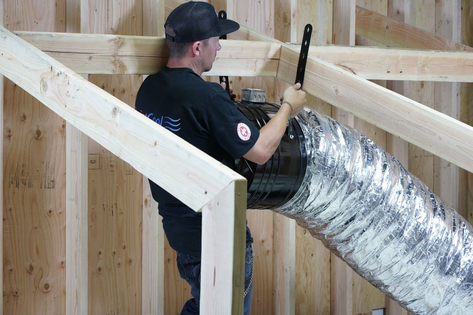 Worker installing a silver duct in a wooden-framed wall under construction