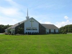 White church with a steeple and cross, set on a green lawn under a blue sky
