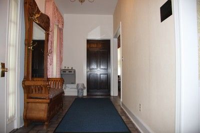 Narrow hallway with dark blue carpet, wooden bench, white walls, and a dark door at the end