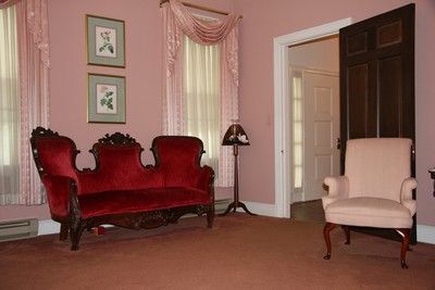 Elegant living room with a red loveseat, cream armchair, pink walls, and a dark wooden cabinet