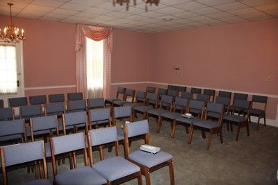 Empty meeting room with rows of blue chairs and pink walls, lit by windows and chandeliers