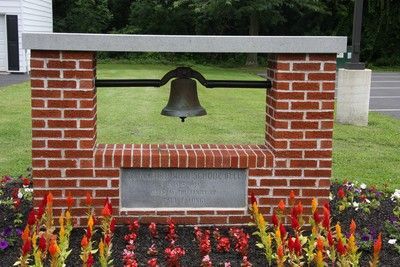 Brick memorial bell in a flower bed with red and yellow flowers