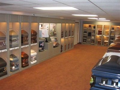 Indoor storage room with rows of stacked caskets on shelves and floor displays