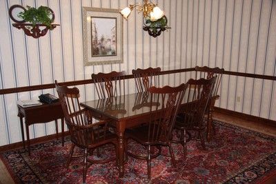Dining room with a wooden table and chairs, striped wallpaper, red patterned rug, and hanging plants and lamp.