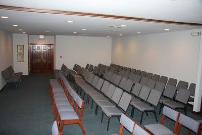 Empty conference room with rows of gray chairs facing the front and wooden chairs along the side walls