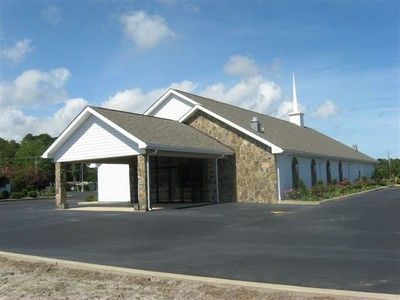 Small stone building with white roof overhang and a paved parking lot under a blue sky