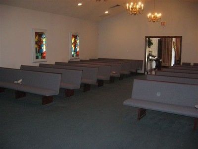 Empty church sanctuary with wooden pews, stained-glass windows, and chandelier lighting