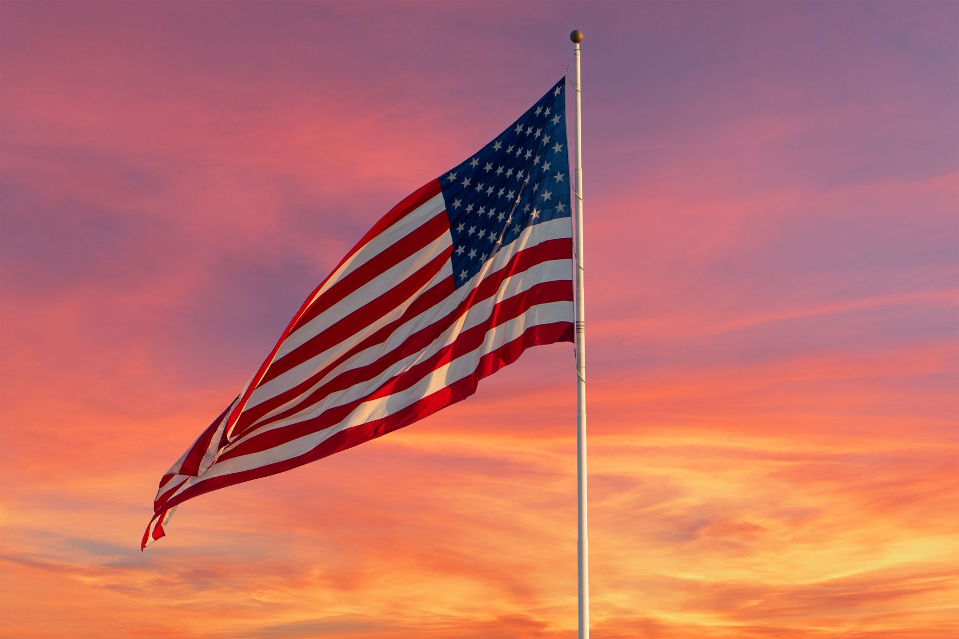 American flag waving on a pole against a vivid orange and pink sunset sky