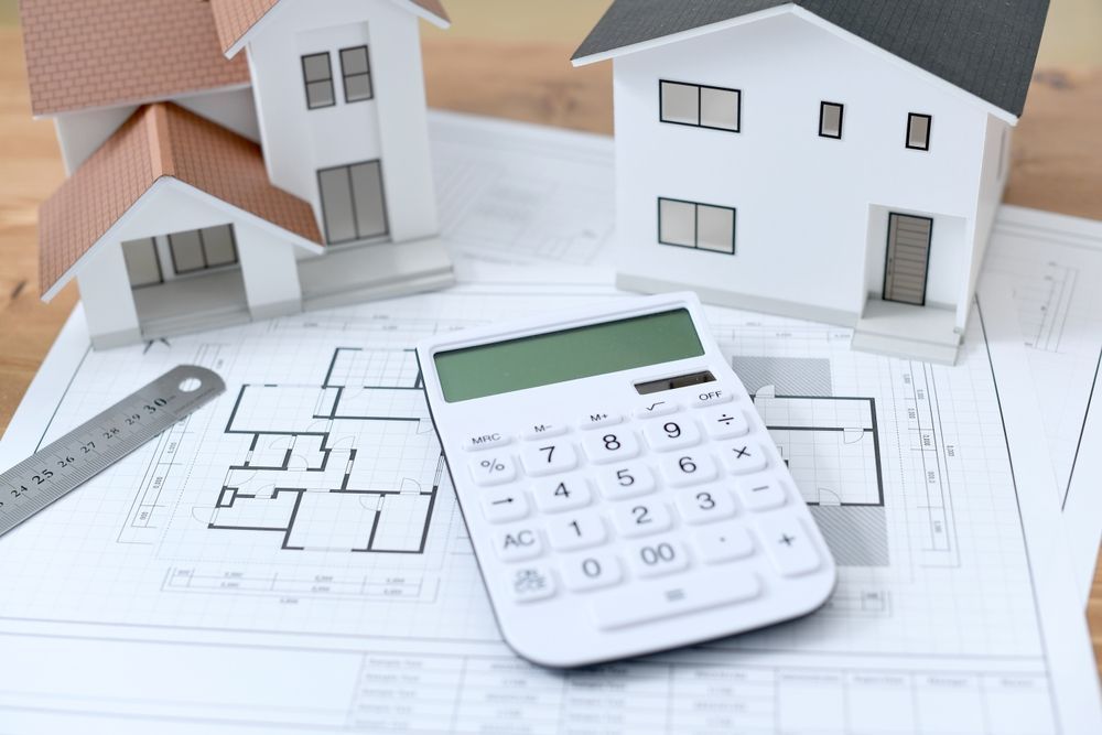 Houses, floor plans, a calculator, and a ruler on a desk, suggesting home construction budgeting.