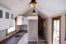 Bright narrow kitchen with white cabinets, wood countertops, and a small stairway or loft area.