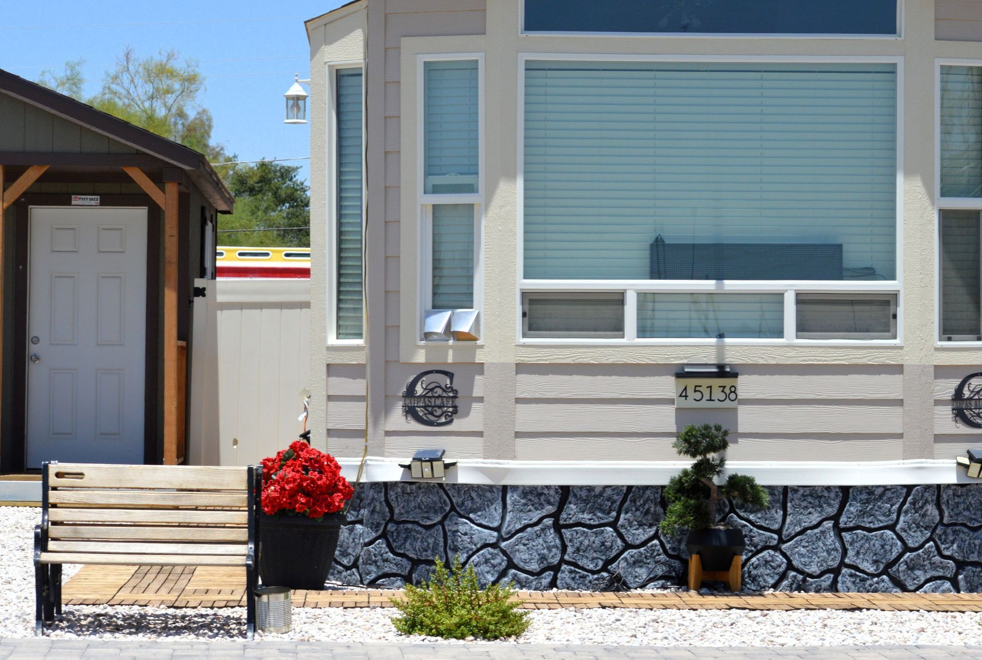 Single-story house with beige siding, blue shutters, stone wall, and red flowers by the front steps
