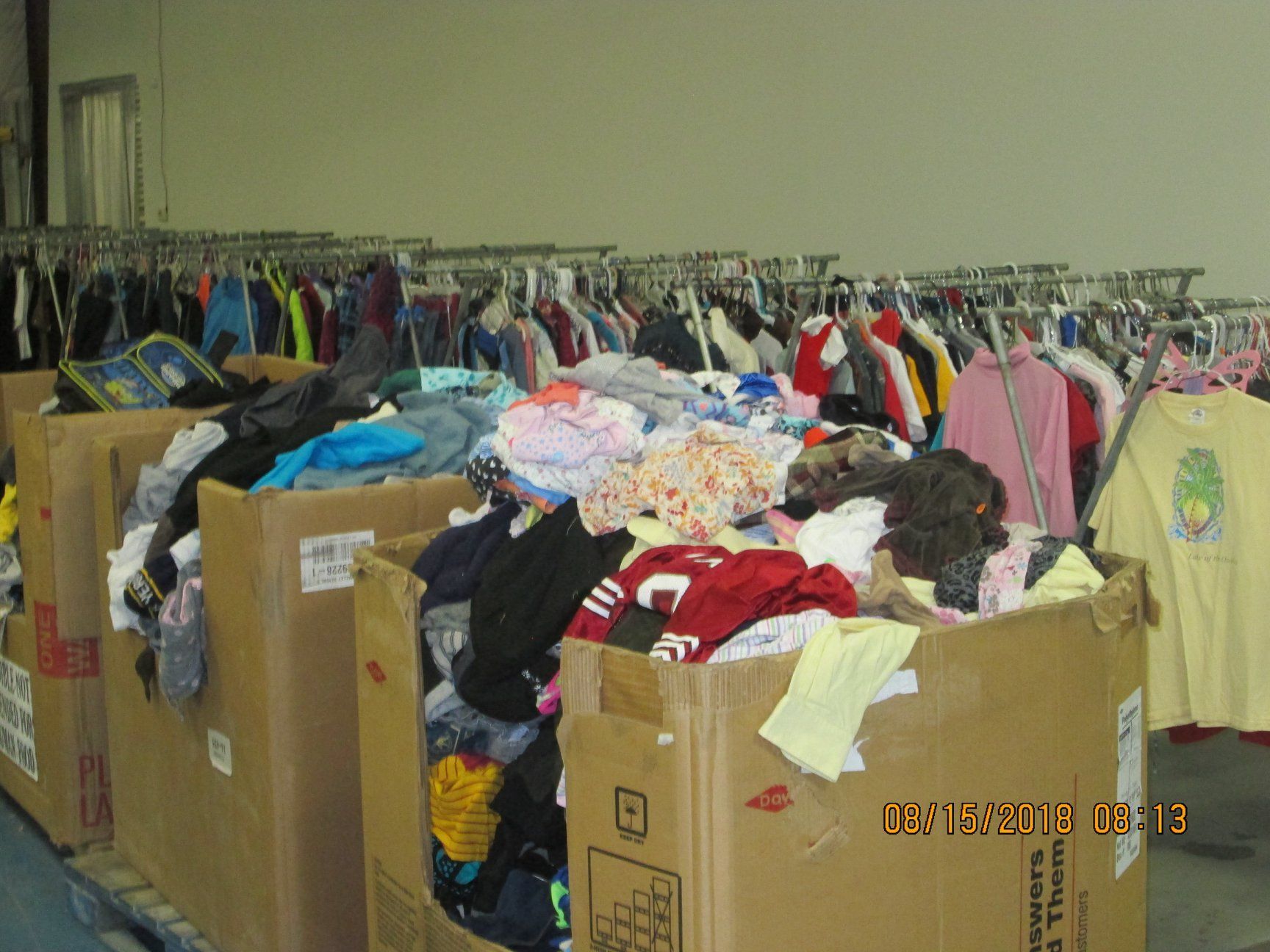 Cardboard boxes overflowing with clothing, clothing racks in background. Warehouse setting. Cardboard boxes overflowing with clothing, clothing racks in background. Warehouse setting.