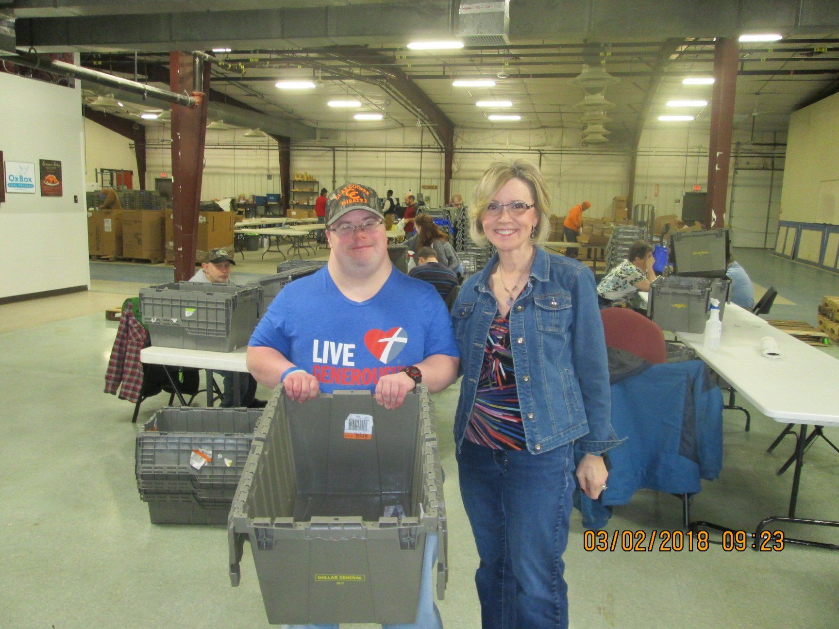 Man with Down syndrome and woman pose with a box in a warehouse setting, smiling at the camera. Man with Down syndrome and woman pose with a box in a warehouse setting, smiling at the camera.